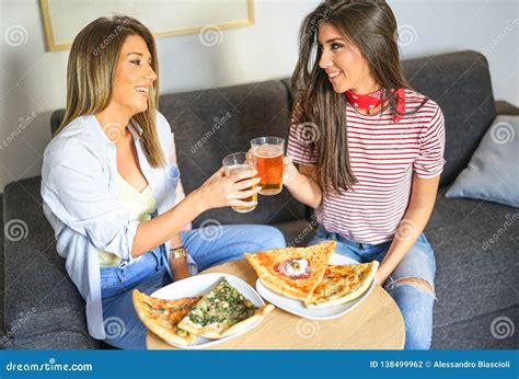 Young Women Having A Lunch Together Toasting Beers And Eating Pizza