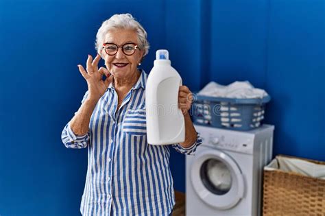 Senior Woman With Grey Hair Holding Detergent Bottle Doing Ok Sign With