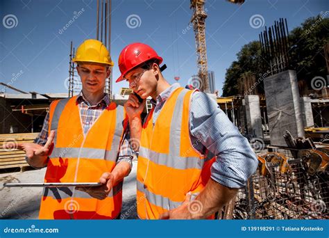 Structural Engineer And Architect Dressed In Orange Work Vests And Hard