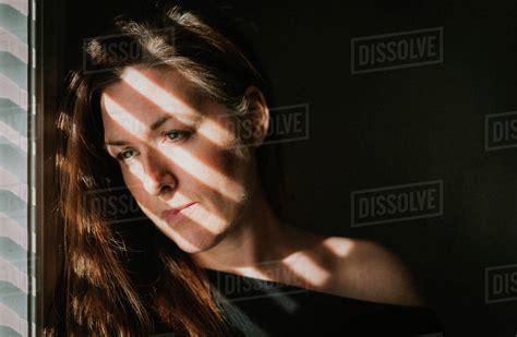 Portrait Of Woman Looking Out Window With Shadows Across Her Face