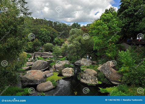 Huge Boulders Lie In The River Among High Green Trees Against The Blue