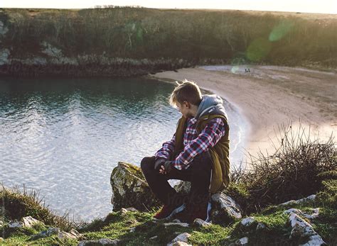 A Teenage Boy Sitting Above A Beautiful Beach Looking Away From