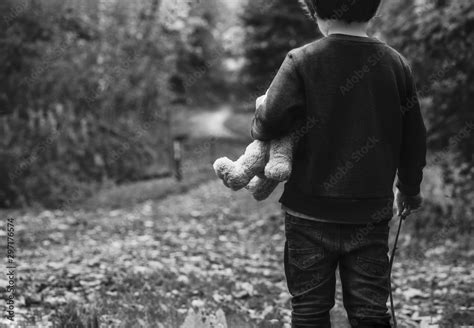Black And White Photo Of Kid Holding Teddy Waking Alone In The Forest