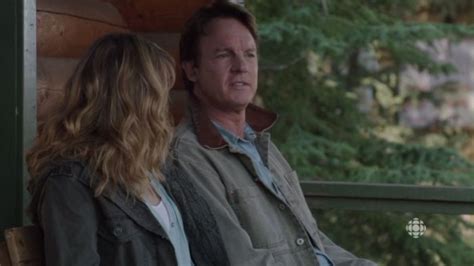 A Man Sitting Next To A Woman On Top Of A Wooden Bench In Front Of Trees