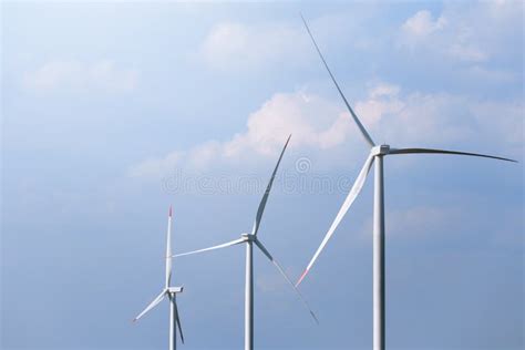 Farm Of Windmill Turbines On Agricultural Field With Blue Sky In