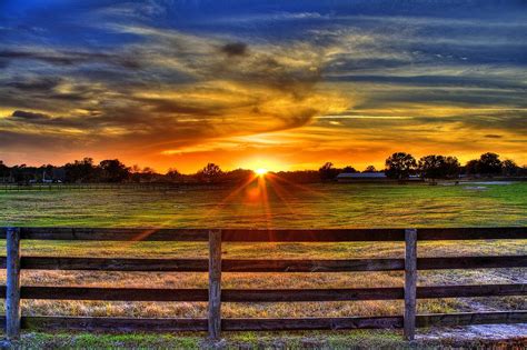 The Sun Is Setting Over A Field With A Wooden Fence In Front Of It