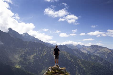 Man In Black T Shirt Standing On Mountain Cliff Under Blue Sky Hd