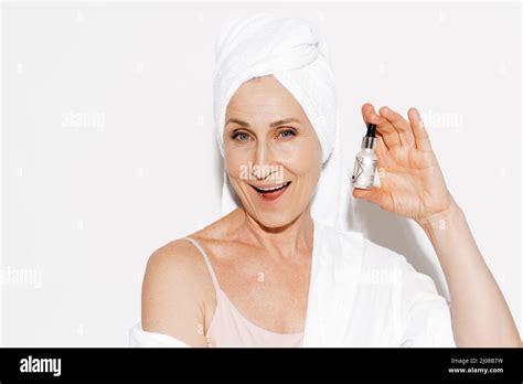 Mature Woman Wrapped In Shower Towel Smiling While Showing Face Serum
