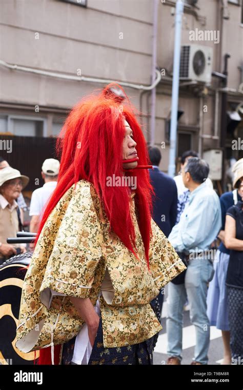 japanese man in vibrant red wig and chin straps dressed as oni ogre demon in the sanja