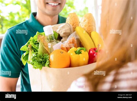 Smiling Delivery Man Giving Grocery Bag To Woman Customer At Home For