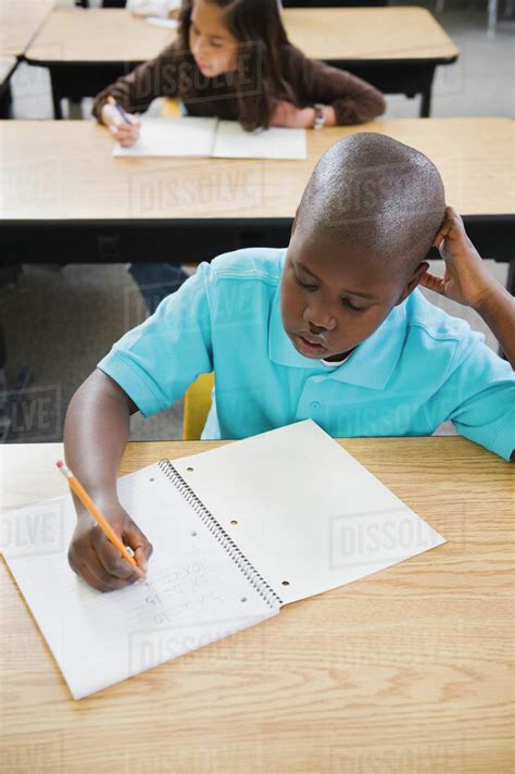 Elementary Students Writing In Notebooks At Their Desks Stock Photo