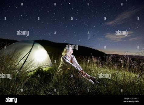 Female Traveler Sitting On Grass Enjoying Fantastic View Of Night Sky