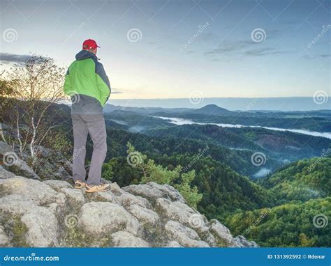 Man Stands On The Peak Of Rock Hiker Watching To Autumn Sun At Horizon