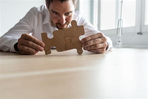 Focused Young Businessman Joining Two Matching Puzzle Pieces Stock