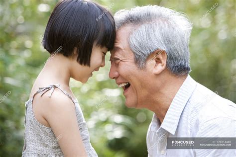 Chinese Grandpa And Granddaughter Pressing Foreheads In Garden — Senior