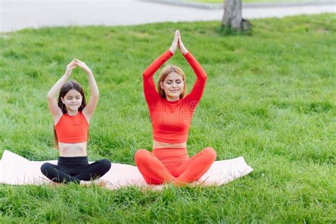 Mother And Daughter Doing Yoga Exercises On Grass In The Park At The