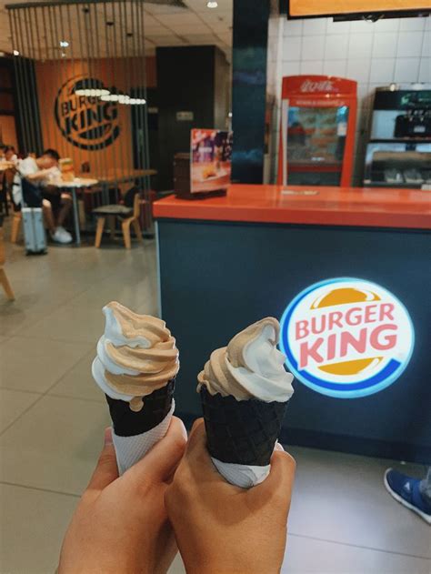A Person Holding Two Cupcakes In Their Hands At A Fast Food Restaurant With The Burger King Logo