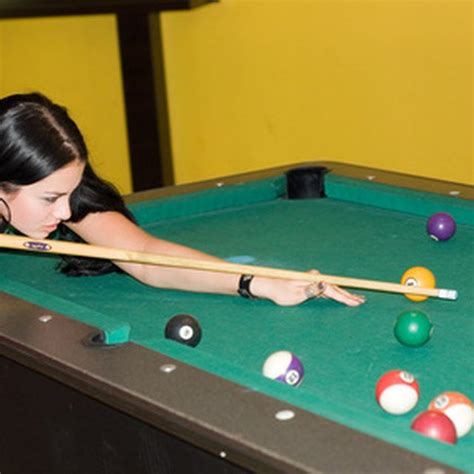 two women are playing pool on a green table