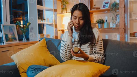 Sick Young Asian Woman Hold Medicine Sit On Couch Use Smart Phone To Consult With Doctor At Home