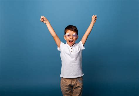 Premium Photo Happy Little Boy Triumphant With Raised Hands On A Blue