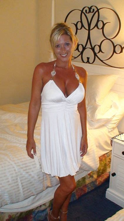 A Woman Standing In Front Of A Bed Wearing A White Dress And High