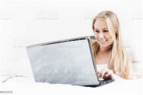 Beautiful Blonde Woman Smiles As She Uses Her Laptop Computer In Bed