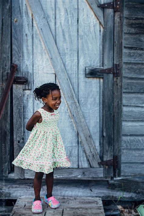 Smilling African American Girl In A Dress By A Wooden Shack By