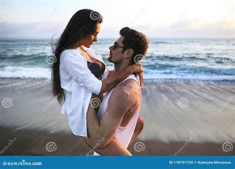 Beautiful Sexy Young Caucasian Couple Cuddling On The Beach At Sunset Time Near Ocean During