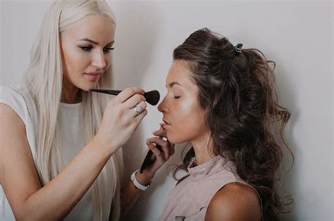 Pretty Makeup Artist Applying Makeup To A Model Against White Wall By Stocksy Contributor