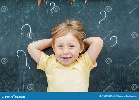 Top View Of A Little Blond Kid Boy With Question Mark On Blackboard