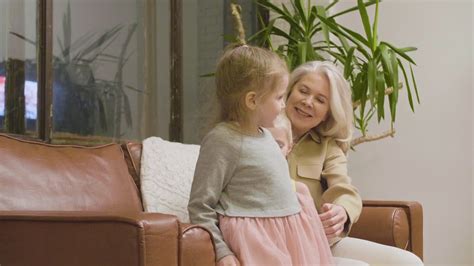 Vídeo de arquivo Gratuito Avó feliz sentada no sofá e abraçando suas duas netinhas em casa