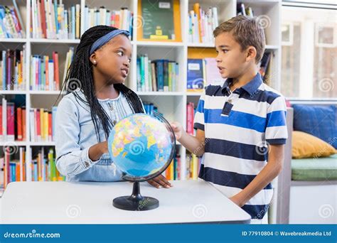 School Kids Discussing With Each Other In Library With Globe On Table