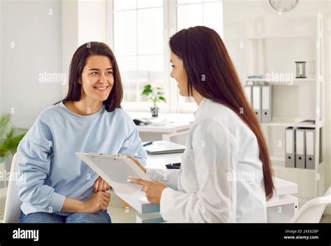 Smiling Female Doctor Talks To Patient And Makes Notes On Card During