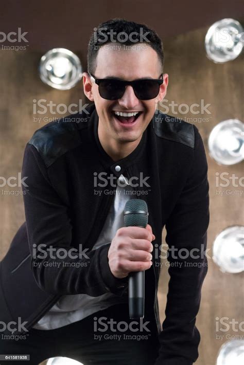 Male Singer In Sunglasses With Microphone Sings In Projectors Lights