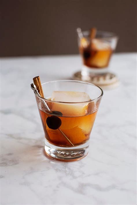 Two Glasses Filled With Drinks Sitting On Top Of A White Marble Counter Topped With Cinnamon Sticks