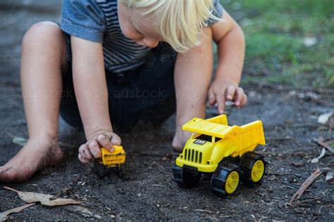 Image Of Cute Little Boy Happily Playing In Black Dirt With Yellow Toy
