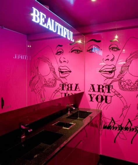 a bathroom with pink walls and graffiti on the wall along with a sink in front of it