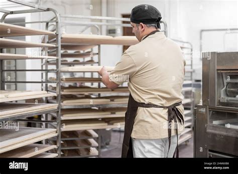 Baker Placing Tray With Formed Raw Dough On Rack Trolley Ready To Bake In The Oven High Quality