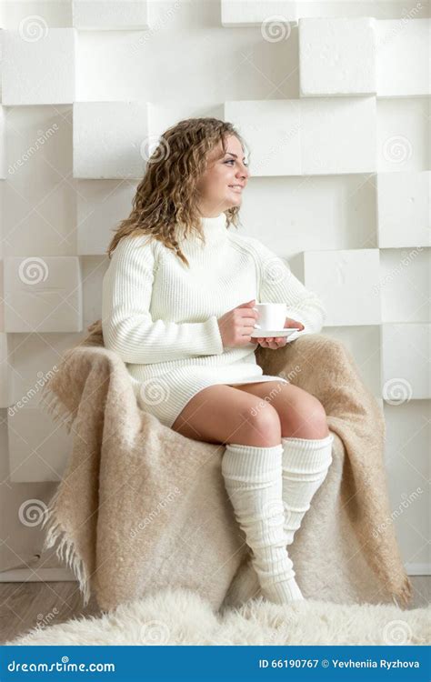 Woman In White Sweater Sitting On Chair And Holding Cup Of Tea Stock