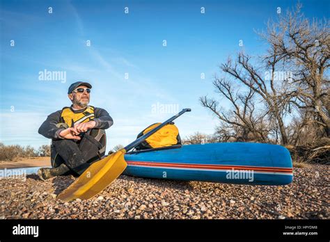 a senior male paddler is taking a rest on a gravelbar during stand up