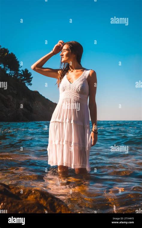 A Young Caucasian Brunette In A White Dress Bathing In The Sea Water