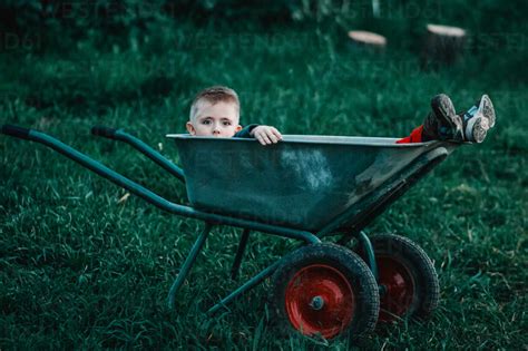 Portrait Of Boy Sitting In Wheelbarrow On Field Stock Photo