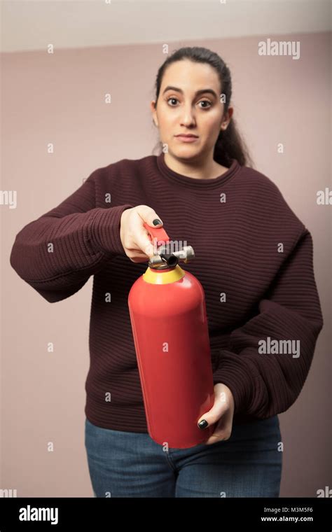 Young Woman Pointing A Red Fire Extinguisher Forwards Towards The Camera With A Serious
