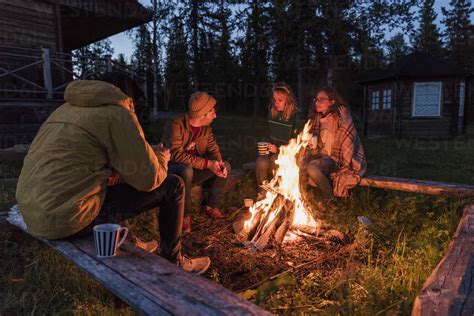 Group Of Friends Sitting At A Campfire Talking And Drinking Tea Stock
