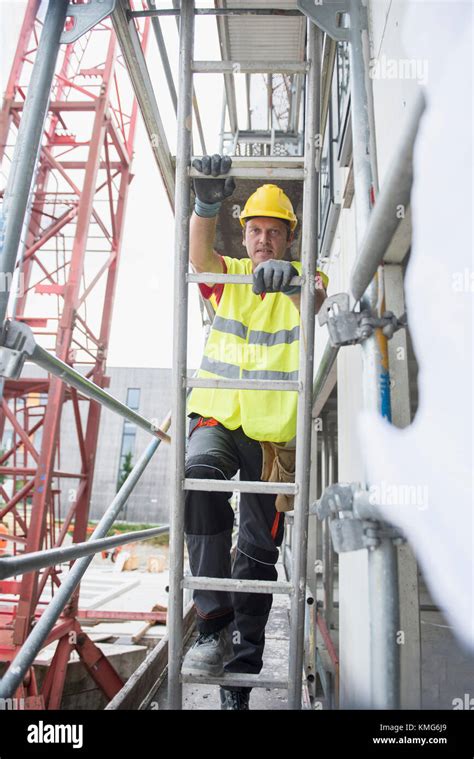 Construction Worker At Building Site Climbing Up A Ladder Stock Photo