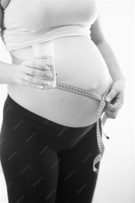 foto em preto e branco de grande plano de uma mulher grávida segurando um copo d água e medindo