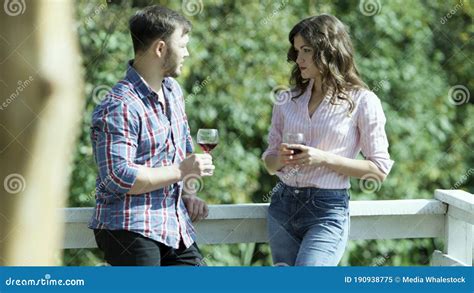 Снаружи вина мужчины и женщины пьет на балконе на фоне зеленой листвы