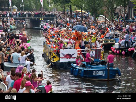 the gay pride parade down a crowded canal lined with people and boats in amsterdam holland