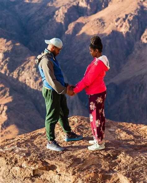 A Man And Woman Holding Hands On Top Of A Mountain