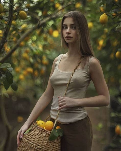 A Woman Holding A Basket Full Of Lemons In Front Of A Tree Filled With